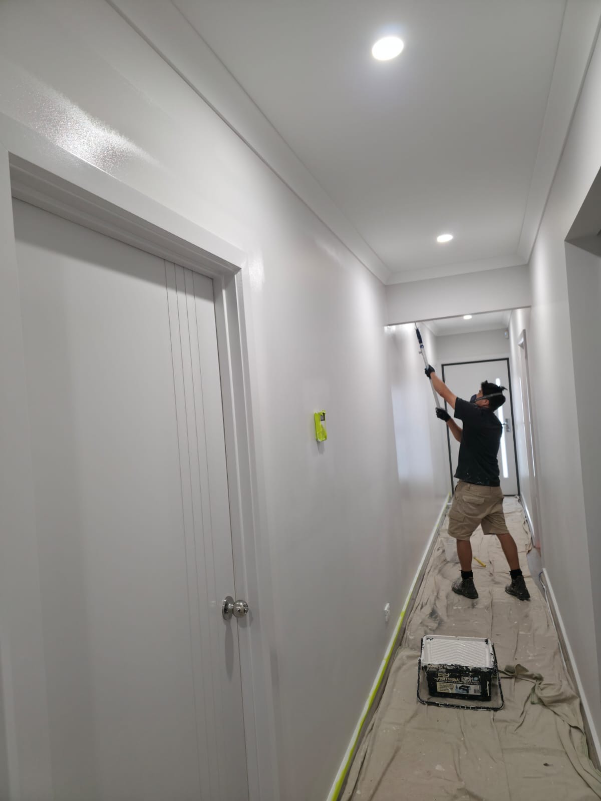 Painter rolling the hallway ceiling with floors covered and edges taped